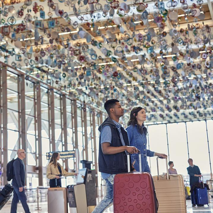 Passengers arriving in the KCI Airport check-in lobby, with colorful artwork adorning the ceiling.
