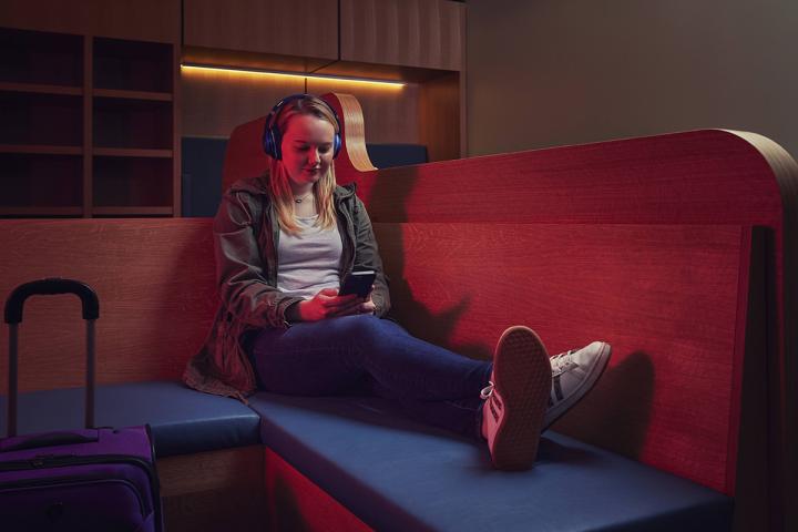 Girl wearing headphones and looking at her cellphone sitting in a darkened sensory room.