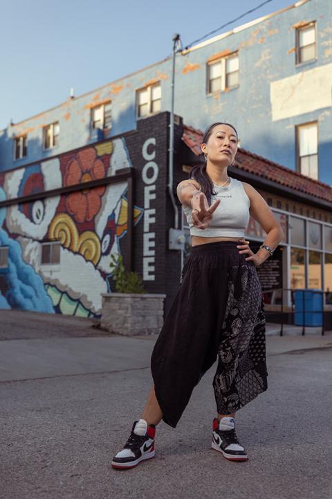 Jackie Nguyen, owner of Café Cà Phê, standing outside her business in front of a Coffee mural
