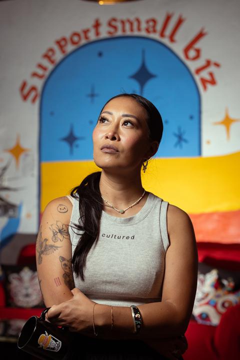 Jackie Nguyen, owner of Café Cà Phê, posing in front of a "Support Small Biz" mural