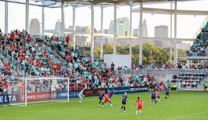KC Current women's soccer team playing, with the stands full of fans and the KC skyline in the background