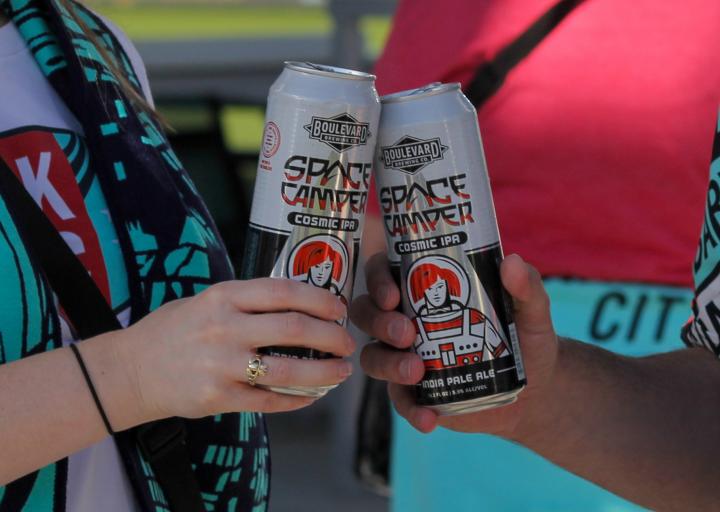 Two people in KC Current scarves cheers-ing Boulevard Space Camper IPA beers