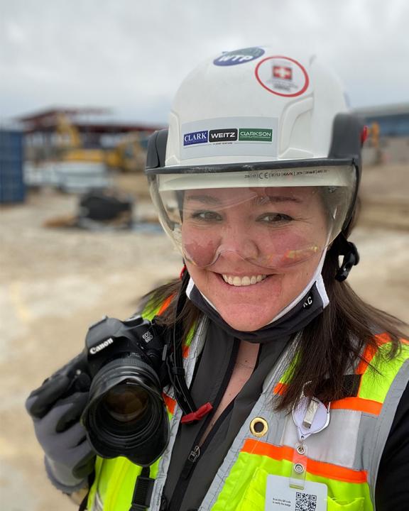 Photographer Kate Sweeten holding a camera while wearing construction site gear.