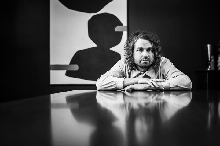 Kevin Morby sitting at and leaning forward on a table, in black and white