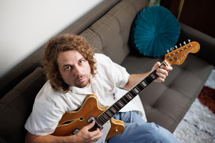 Kevin Morby sitting on a couch playing a guitar