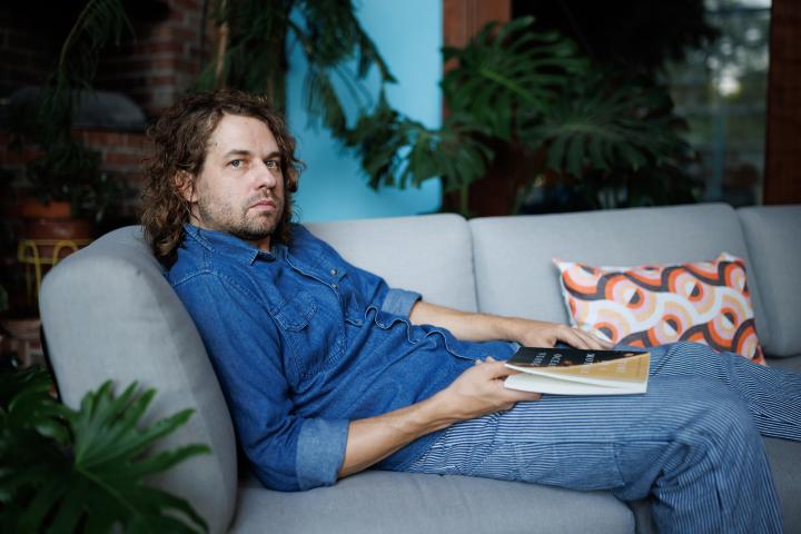 Kevin Morby sitting on a light gray couch with a book in his lap