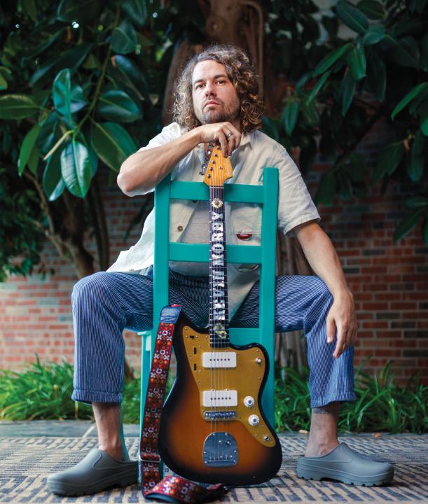 Kevin Morby sitting with his guitar in a turquoise chair