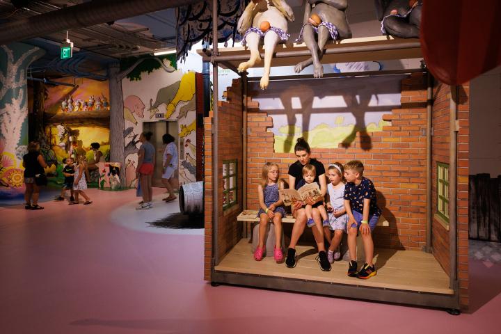 Woman reading a book to several children in a room decorated to look like a storybook