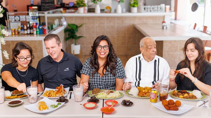 Noeida Kuhnert sitting at a table with family, with a variety of Cuban food on the table.