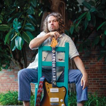 Kevin Morby sitting with his guitar in a turquoise chair